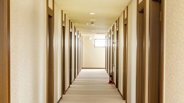 A long, narrow hotel corridor with doors on both sides, a carpeted floor, and a fire extinguisher on the right. - Business Hotel Tsukidate (Kurihara)