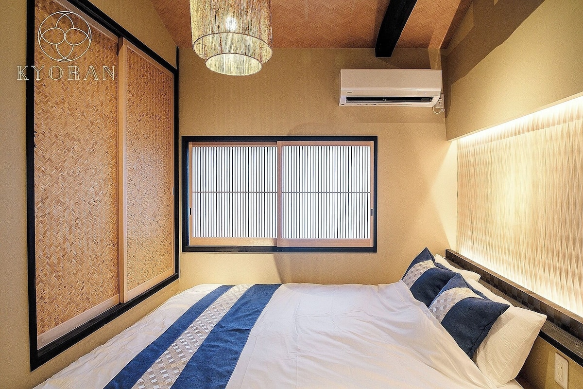 Ein Hotelzimmer mit Bett, Fenster mit vertikalen Jalousien, Klimaanlage und einer Wandverkleidung.