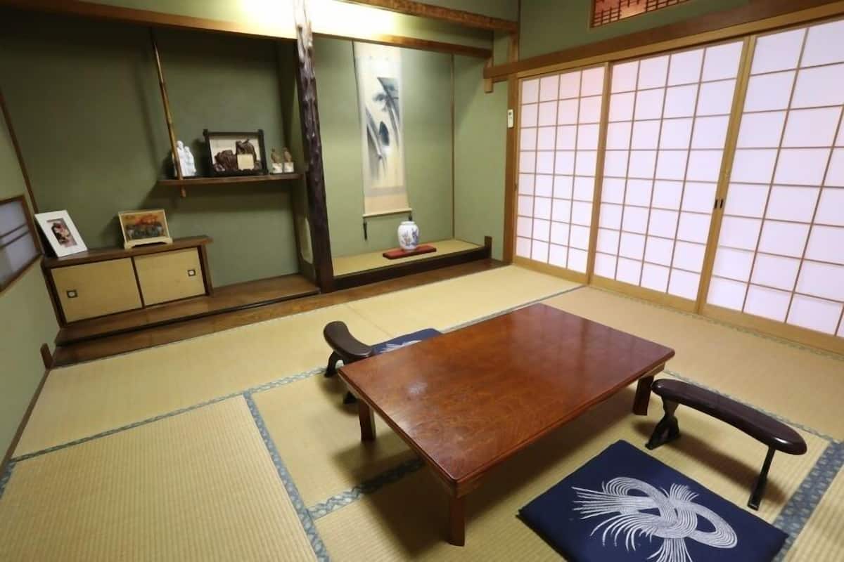 A tatami mat room with a wooden table, benches, a low shelf with items, and a shoji screen door.