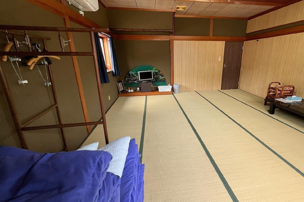 A tatami mat room with a futon bed, a small table with items, and a chair.