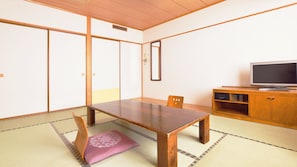 Ein traditioneller japanischer Raum mit Tatami-Böden, einem niedrigen Holztisch, einem Fernseher auf einem Holzständer und Schiebetüren.