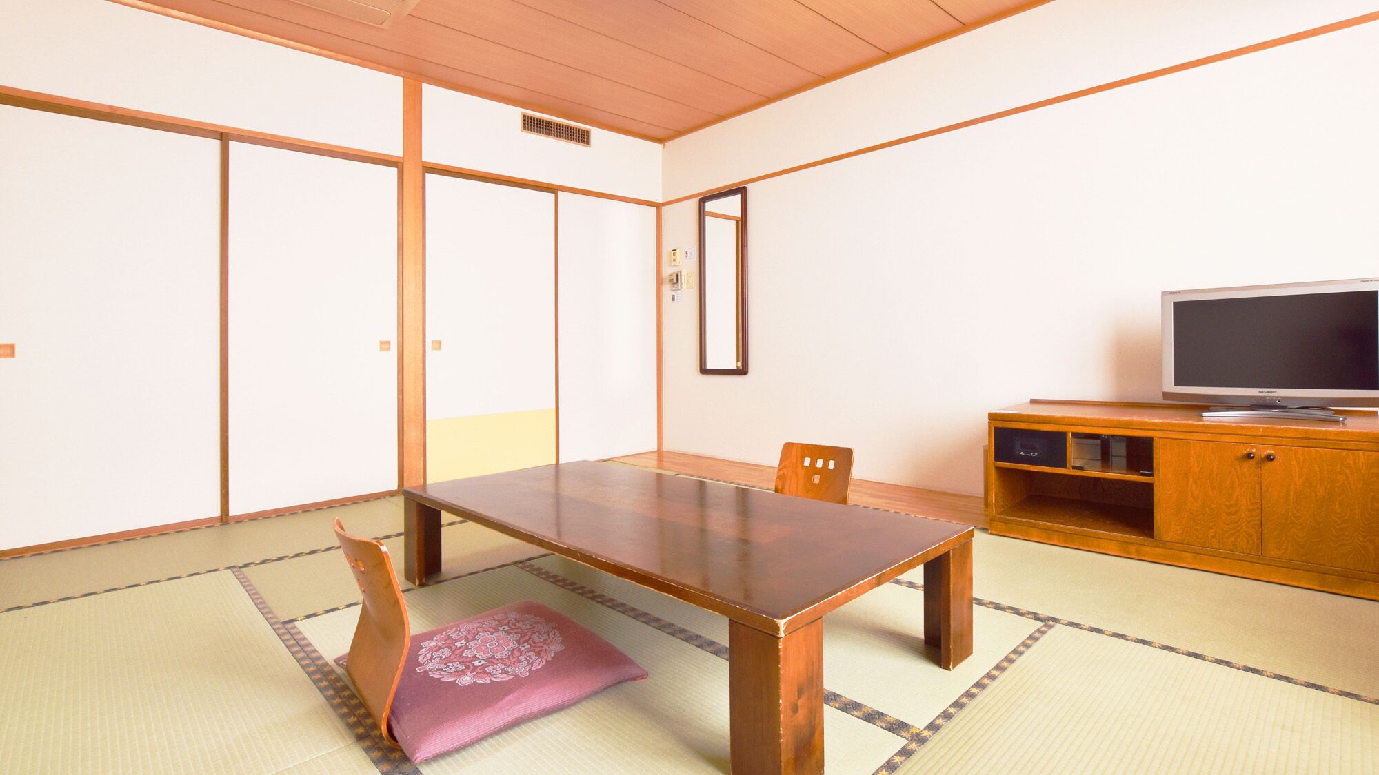 A traditional Japanese room with tatami flooring, a low wooden table, a television on a wooden cabinet, and sliding doors.
