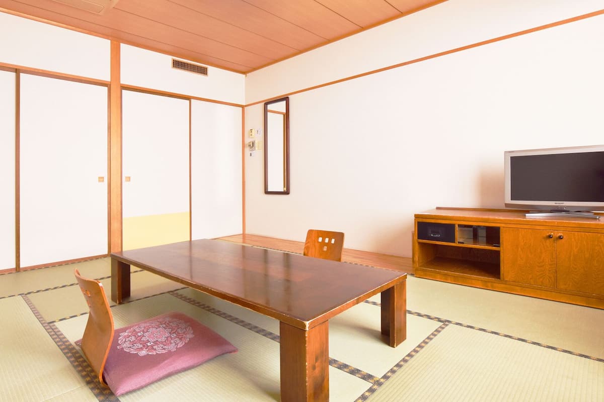 A traditional Japanese room with tatami flooring, a low wooden table, a television on a wooden cabinet, and sliding doors.