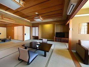 A traditional Japanese-style room with tatami flooring, a low table with cushions, a television, and sliding doors. - Hotel Suiyotei (Atami)