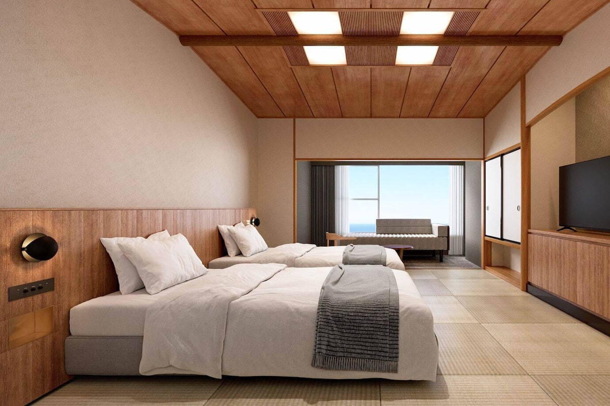 Ein Hotelzimmer mit zwei Betten, einem Fernseher, einem großen Fenster und einer Holzbalkendecke.