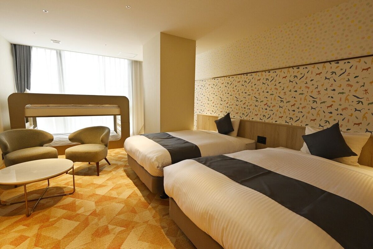 A hotel room with two beds, a sofa, a small table, and a patterned wall.