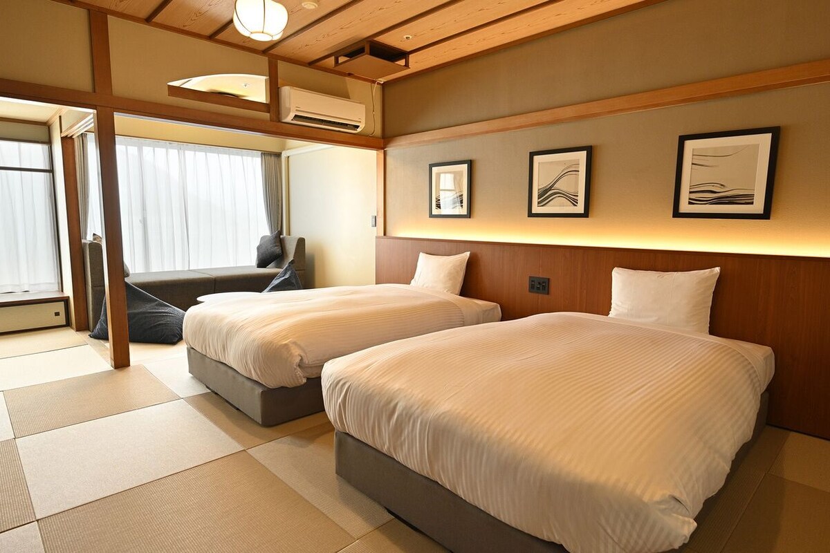 A hotel room with two beds, a desk, and a window with curtains.