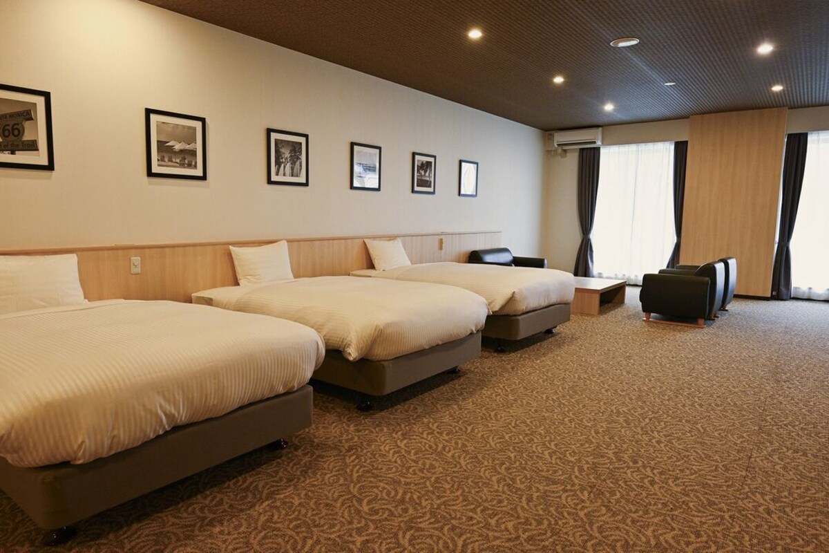 A hotel room with three beds, a desk, and a chair. There are framed pictures on the wall.
