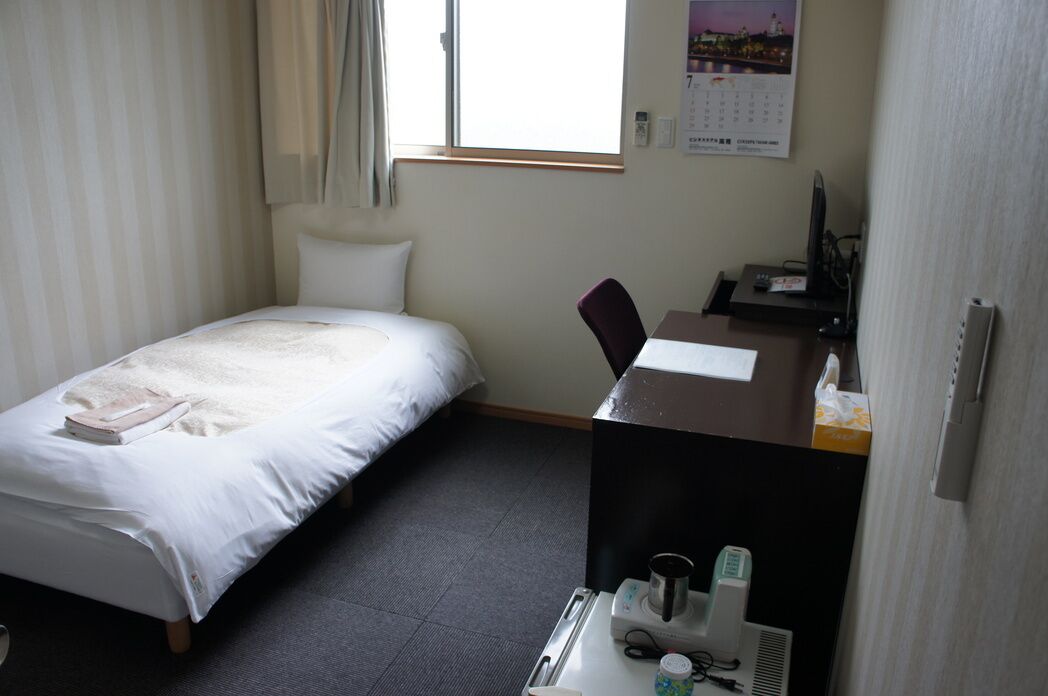 A hotel room with a bed, a desk with a computer, a chair, and a window.