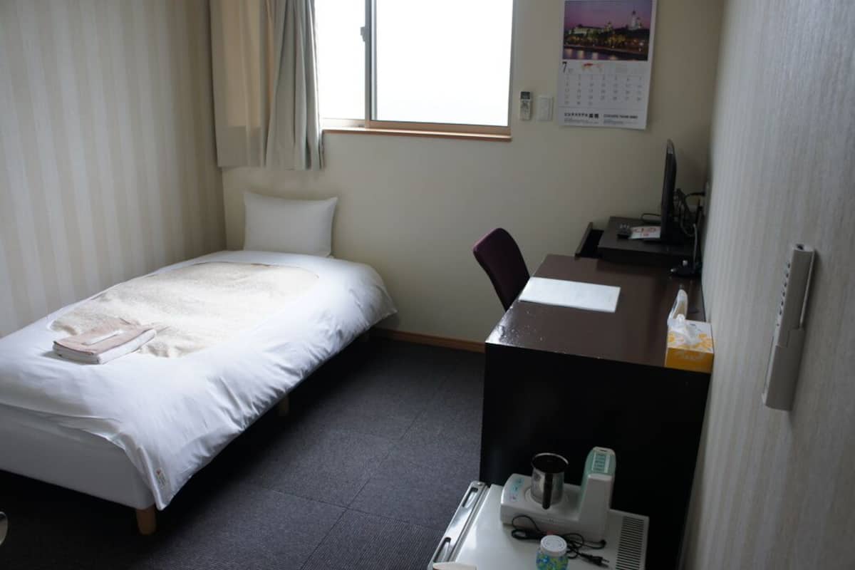Una habitación de hotel con cama, un escritorio con computadora, una silla y una ventana.
