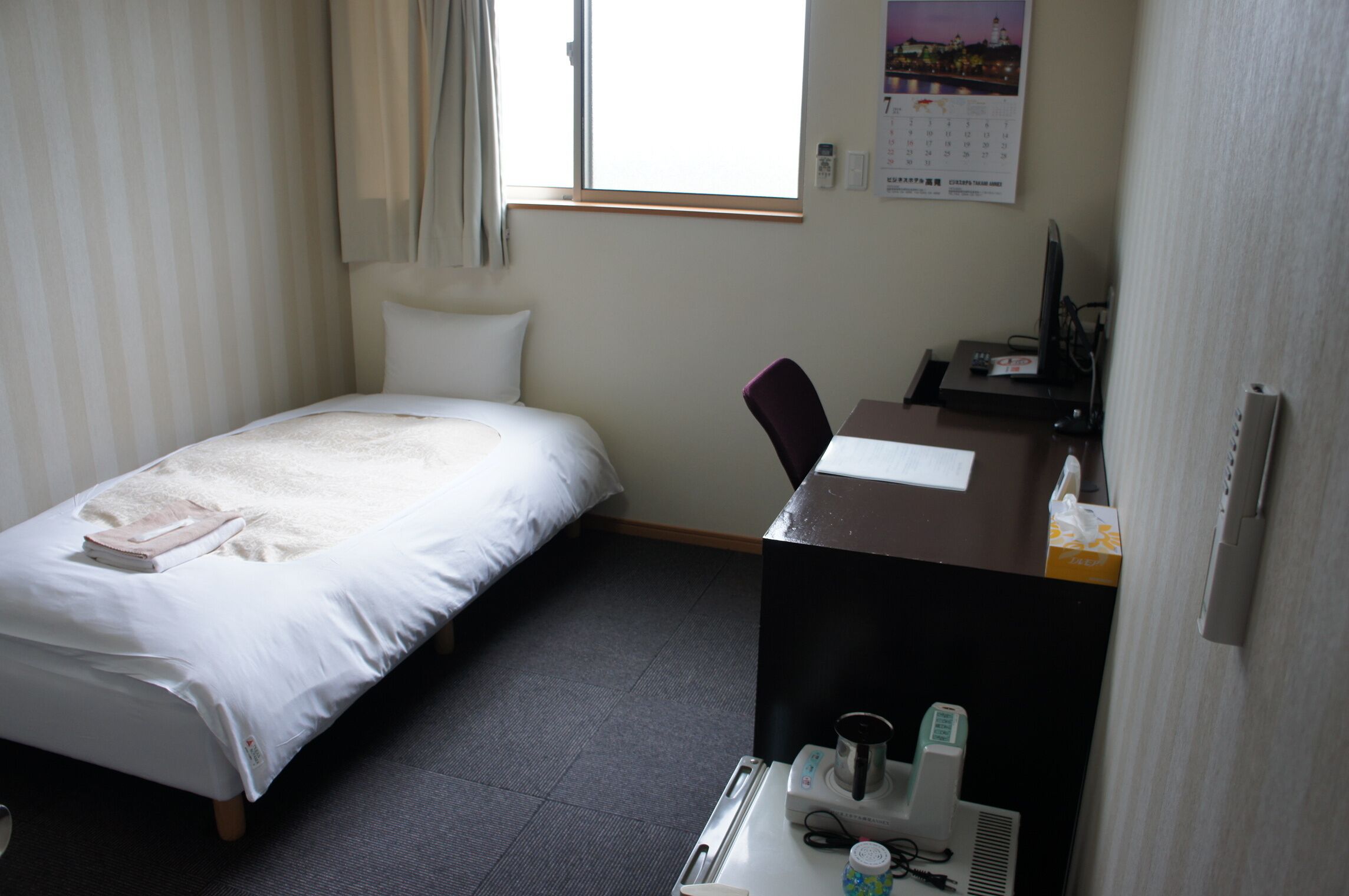 Una habitación de hotel con cama, escritorio, computadora, silla y ventana.