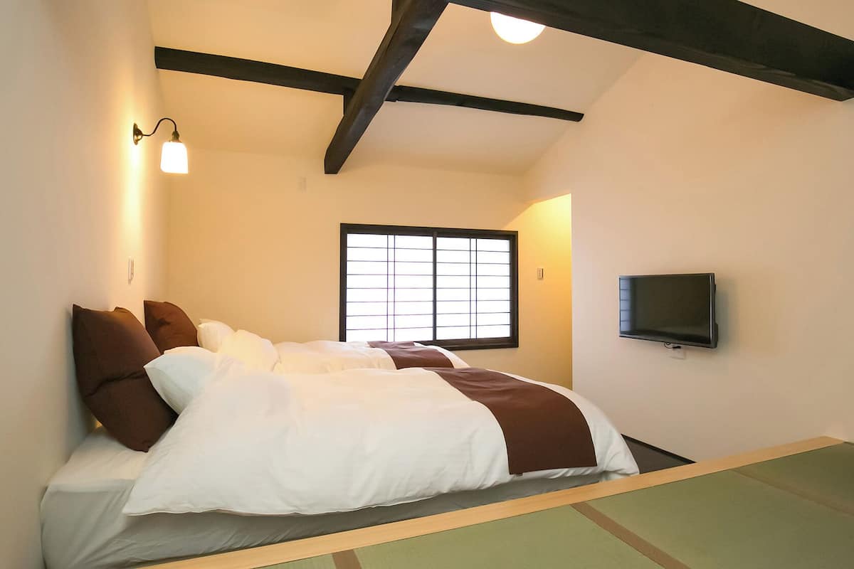Ein Zimmer mit Bett, einem an der Wand befestigten Fernseher und einem Fenster mit Gittermuster.