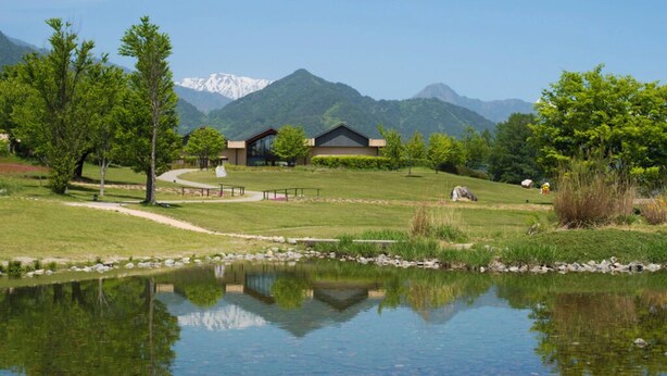 A lakeside view with a building, trees, and mountains in the background. - Suzumushiso (Matsukawa)
