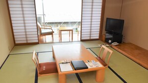 A traditional Japanese room with tatami flooring, a low table, a sofa, a television, and a balcony view. - Suzumushiso (Matsukawa)