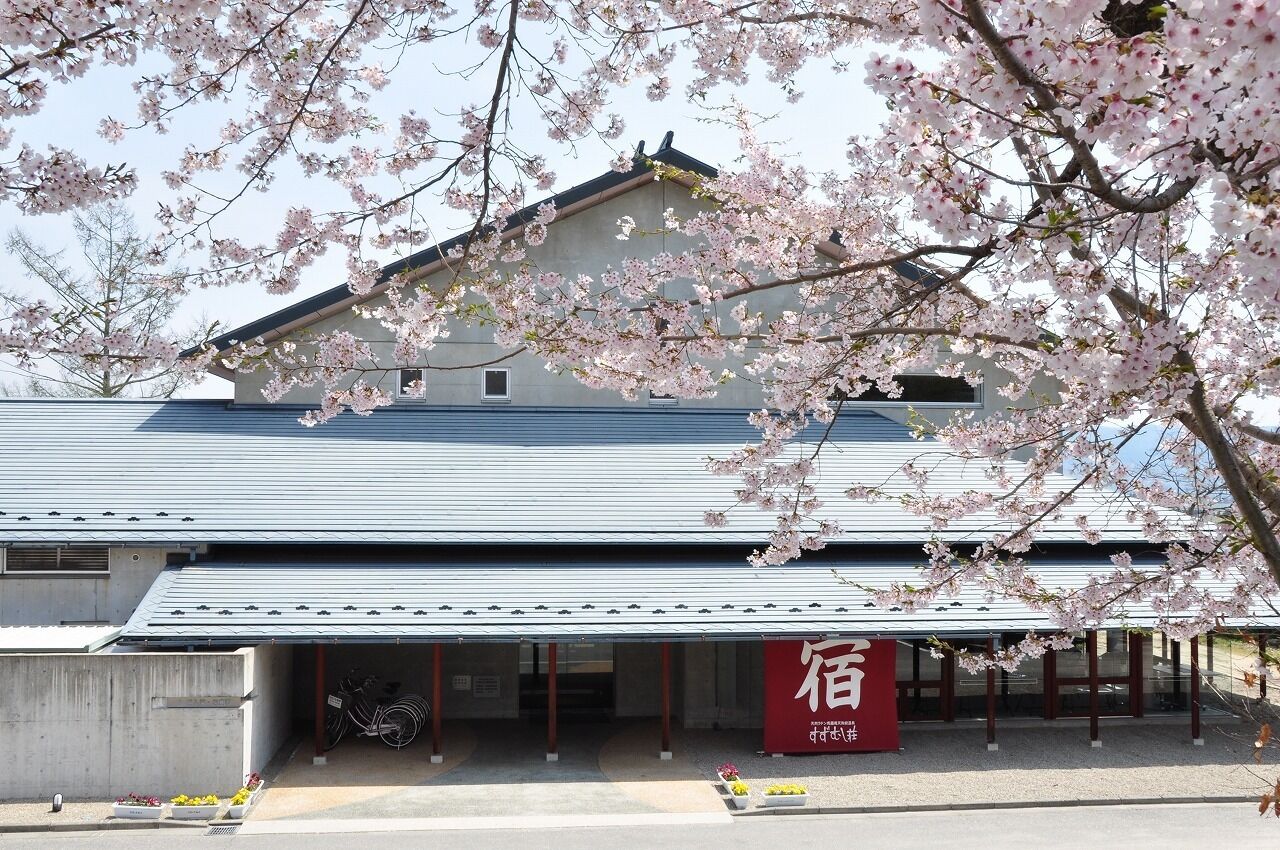 A building with a metal roof, a red sign with white characters, and cherry blossoms in the foreground.