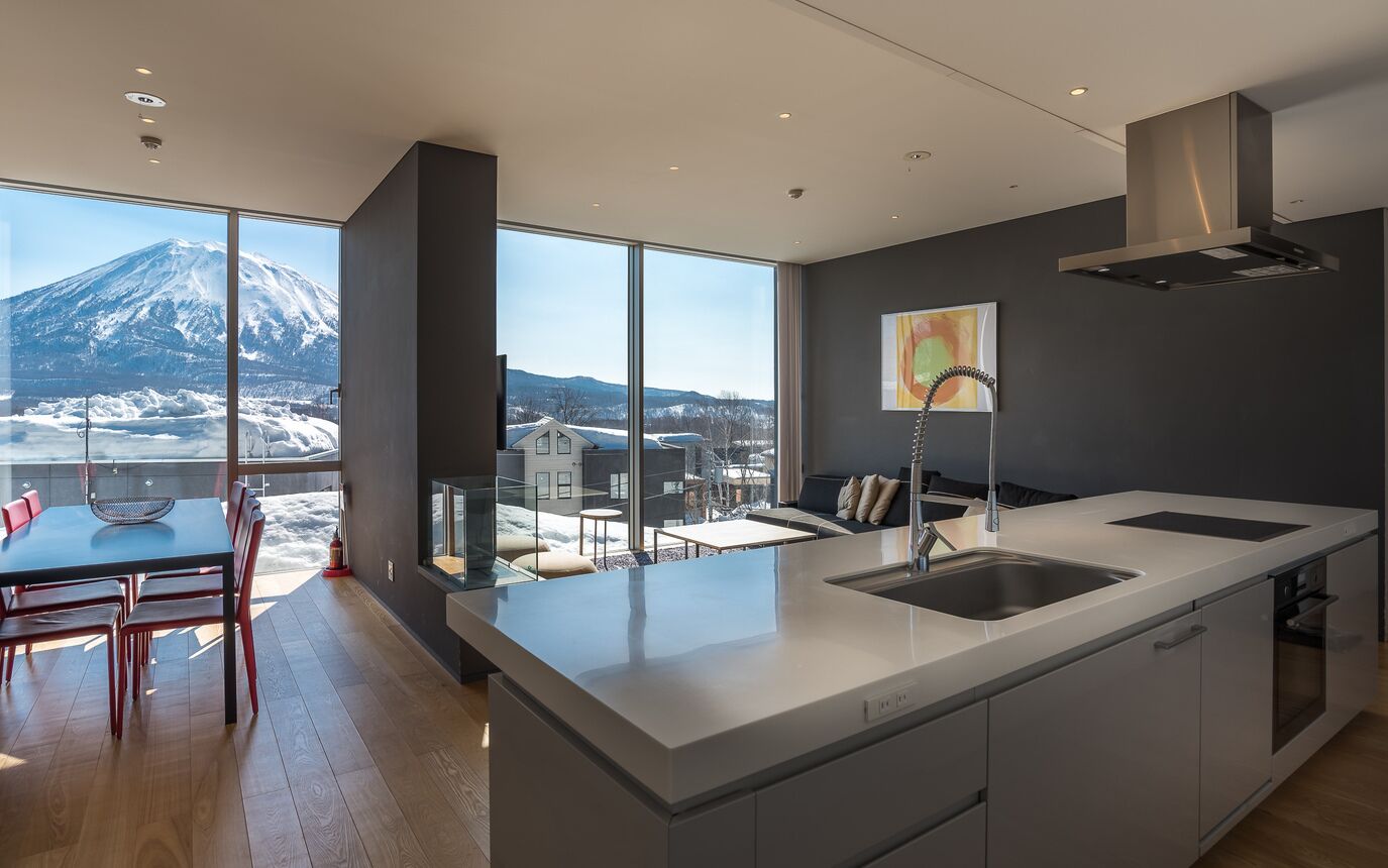 Une cuisine moderne dotée d’un grand îlot central, d’un coin repas offrant une vue sur une montagne enneigée et d’une grande fenêtre.