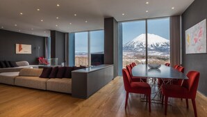 Un intérieur moderne avec un canapé, une table à manger, des chaises et de grandes fenêtres donnant sur une montagne enneigée.