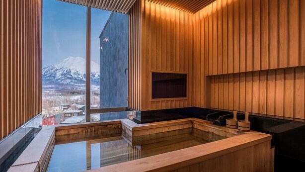 Un sauna moderne avec des murs en bois et une paroi vitrée, offrant une vue sur une montagne enneigée.