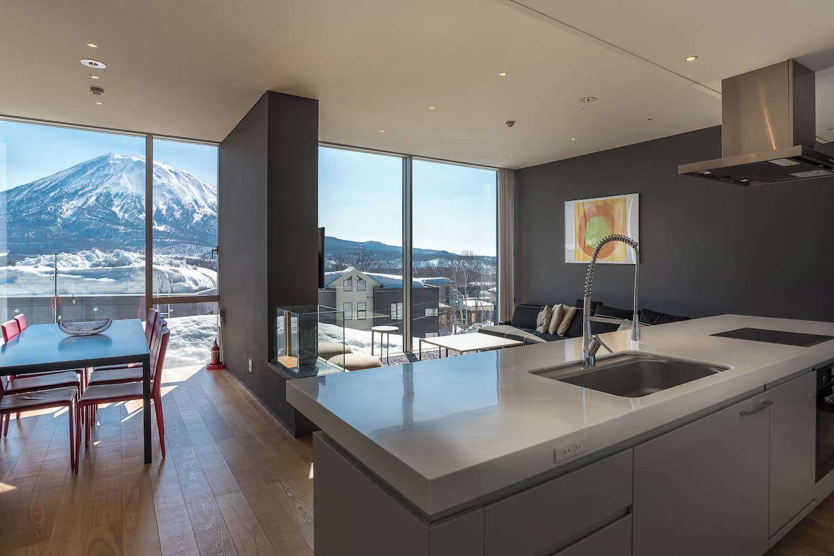A modern kitchen with a large island, a dining area with a view of a snowy mountain, and a large window.