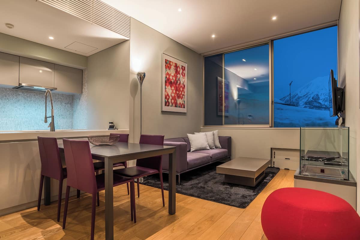 A modern kitchen with a dining area, a sofa, and a large window with a view of a snowy landscape.