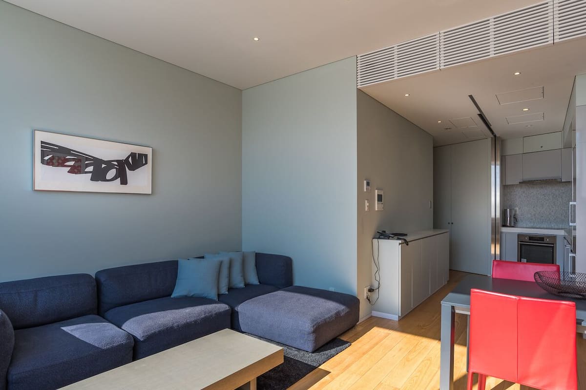 A modern living room with a sofa, a dining table, and a kitchen area in the background.