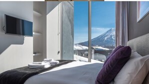 Une chambre d’hôtel moderne équipée d’un lit, d’une télévision et d’une grande fenêtre donnant sur les montagnes.