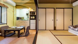 A traditional Japanese-style room with tatami flooring, a low table with chairs, a sofa, and sliding doors. - Kanon House (Kyoto)