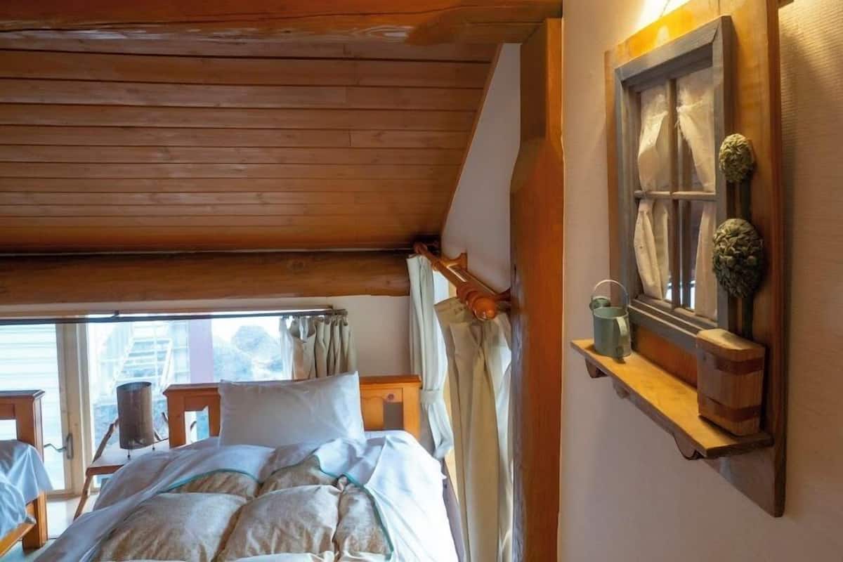 A wooden ceiling, a bed with pillows, a window with curtains, and a shelf with decorative items.