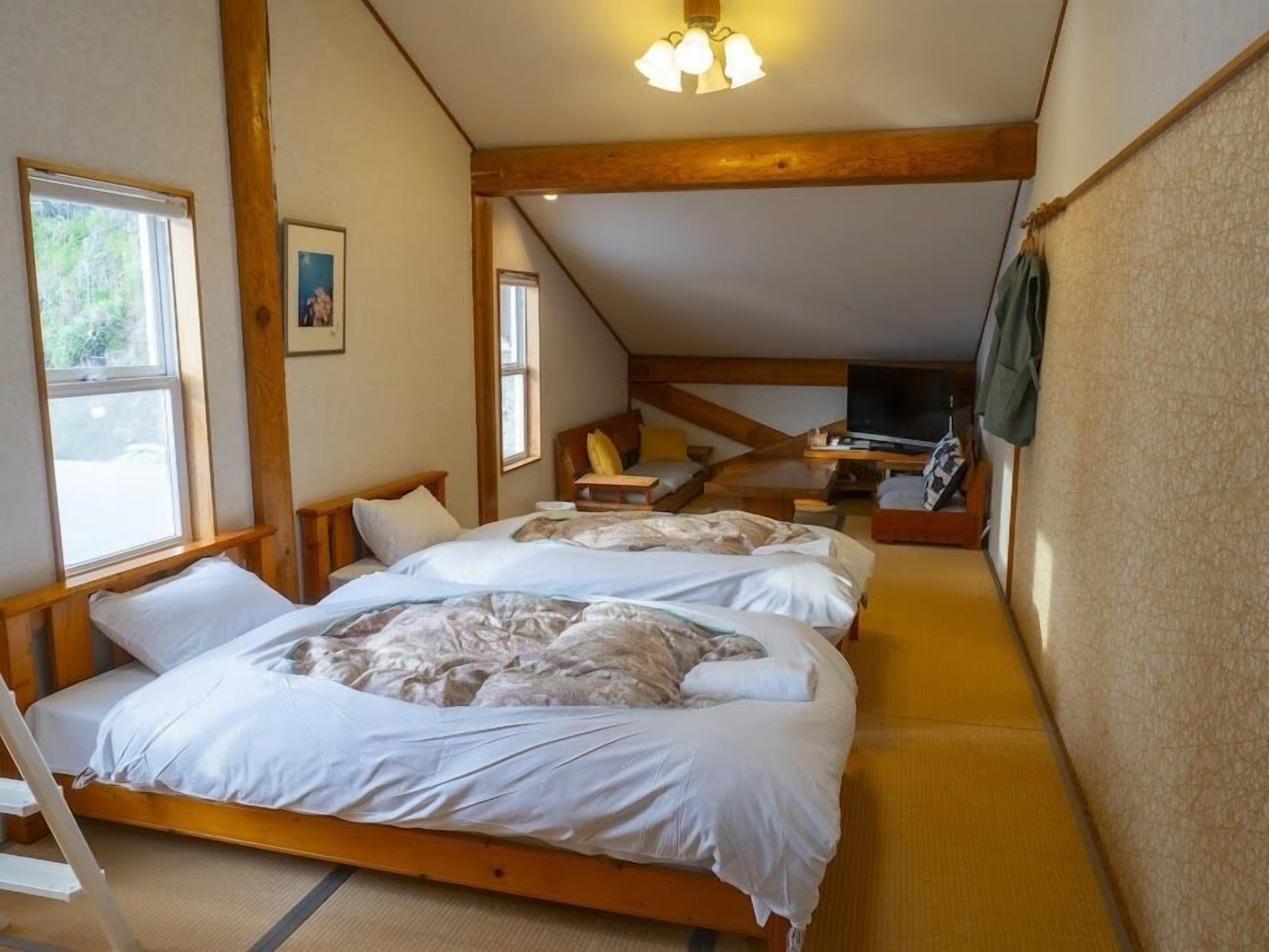 A bedroom with two beds, a TV, and a wooden ceiling structure.
