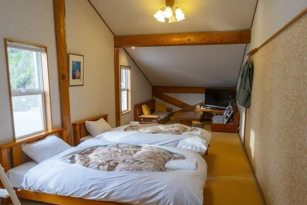 A bedroom with two beds, a TV, and a wooden ceiling structure.