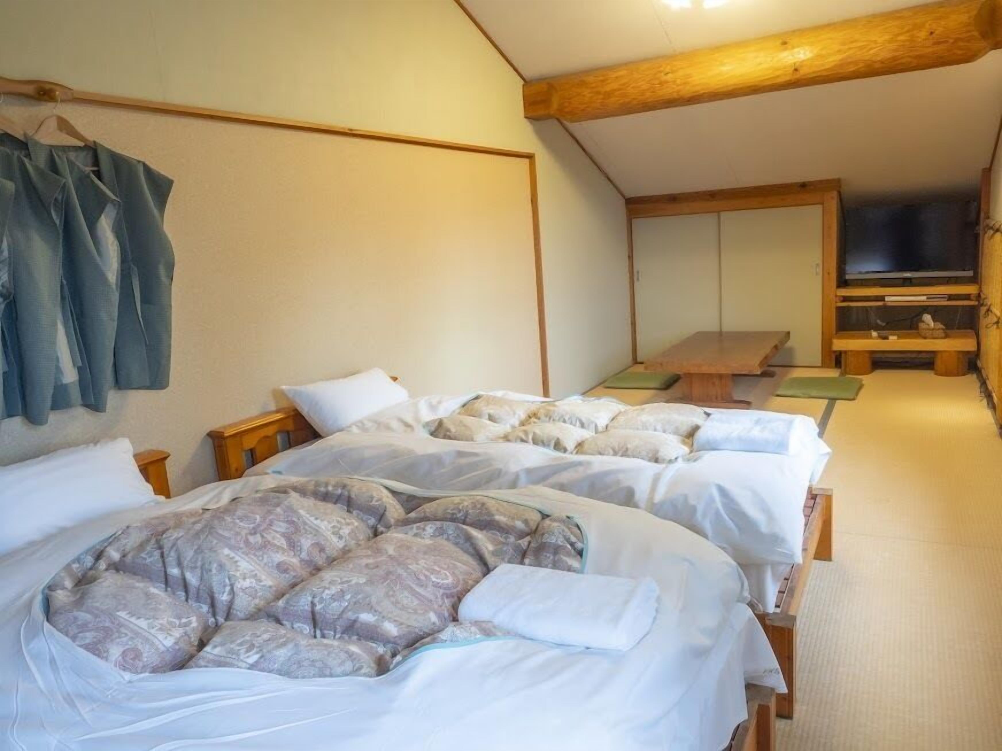 A room with two beds, a wooden ceiling, a TV, and a wall-mounted shelf.