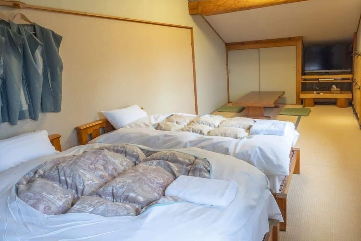A room with two beds, a wooden ceiling, a TV, and a wall-mounted shelf.