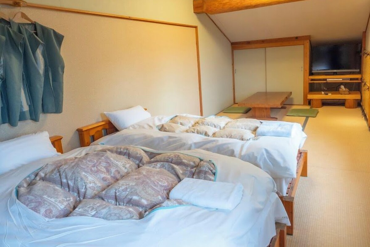 A room with two beds, a wooden ceiling, a television, and a bench.