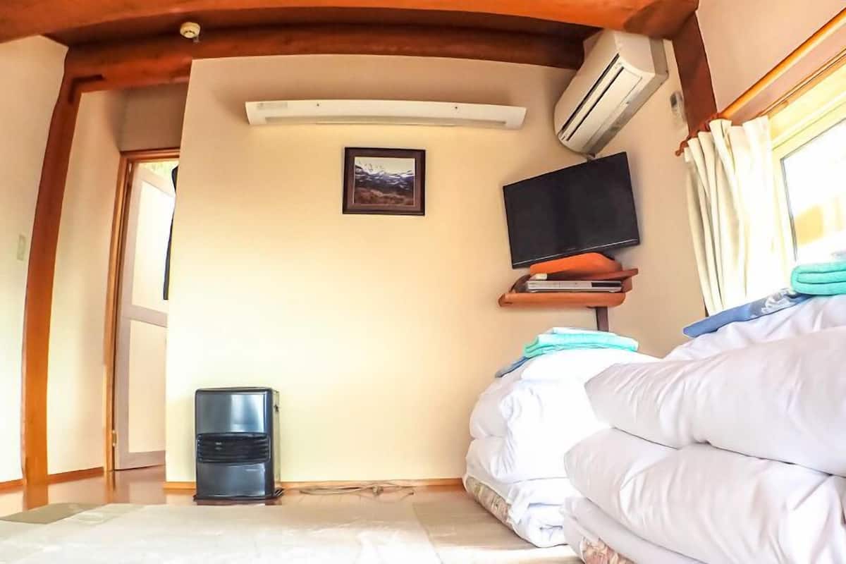 A bedroom with a bed, a TV, an air conditioner, and a window.