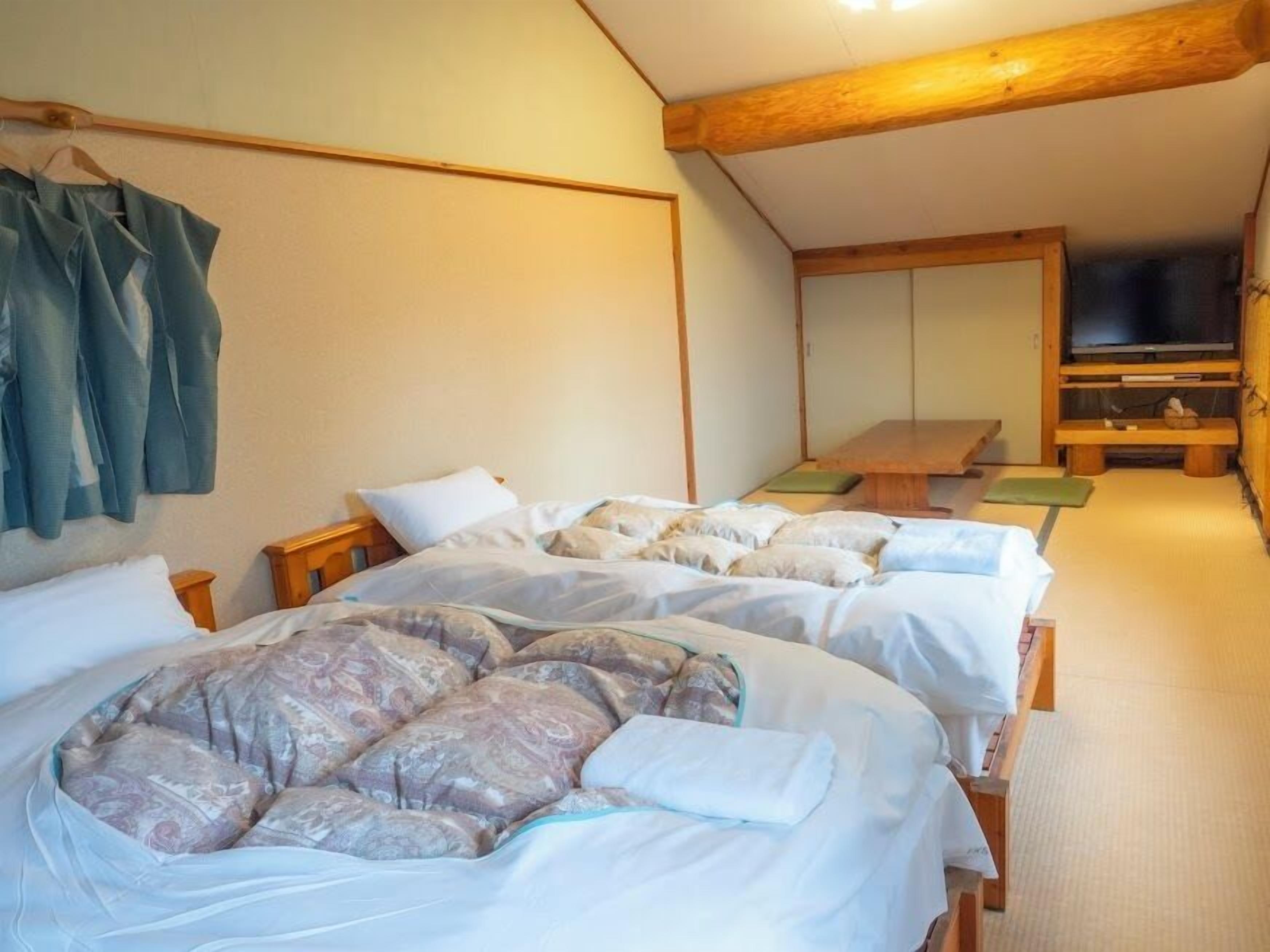 A room with two beds, a wooden ceiling, a television, and a bench.