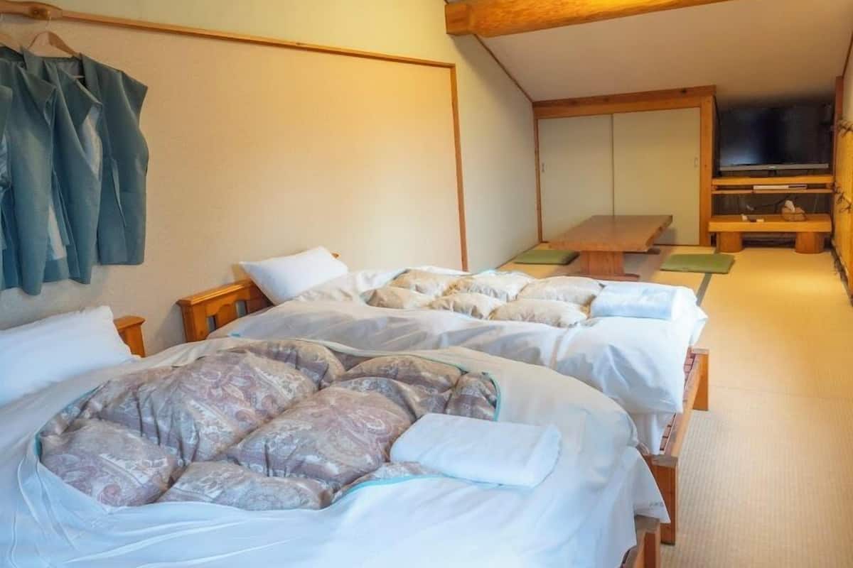 A room with two beds, a wooden ceiling, a television, and a bench.
