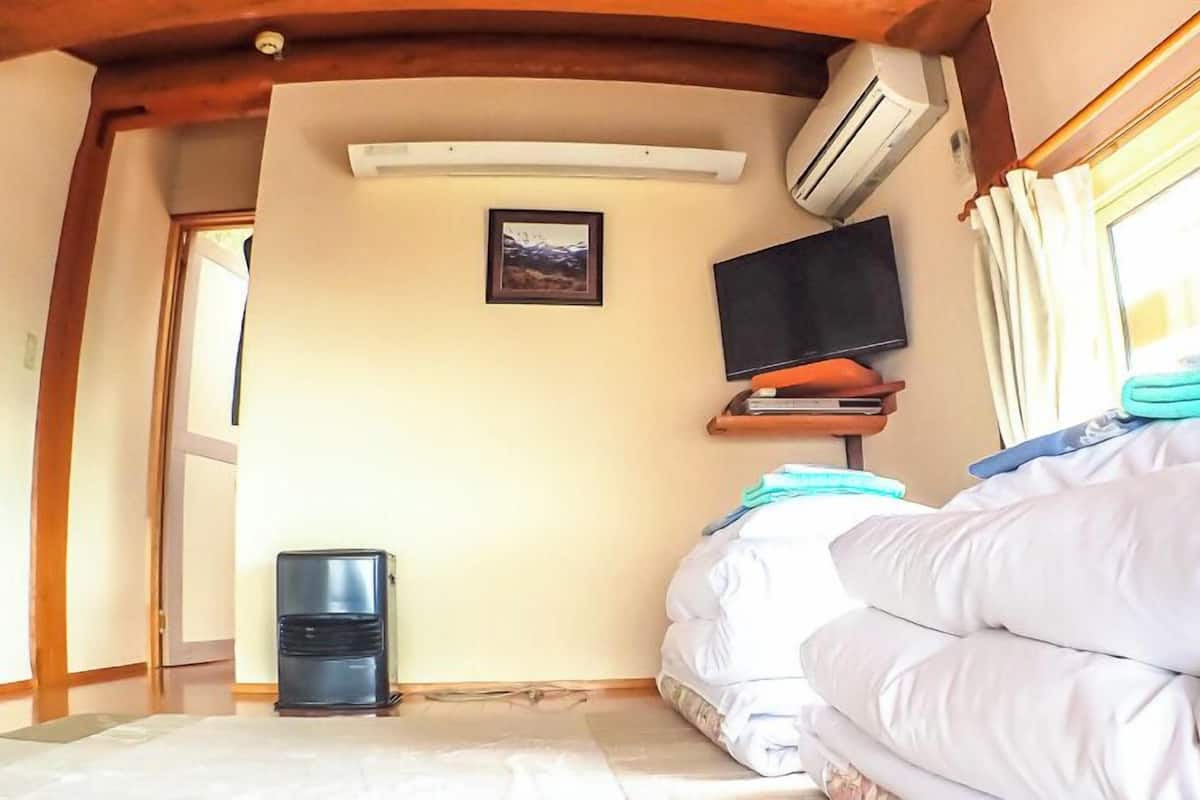 A bedroom with a bed, a TV, an air conditioner, and a window.