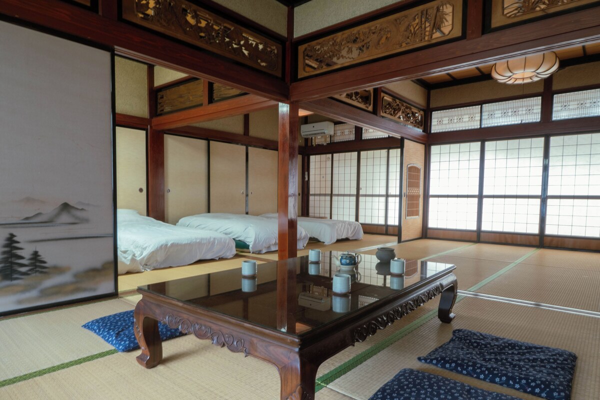 A traditional Japanese room with tatami flooring, a low wooden table, and two tatami mats with pillows.
