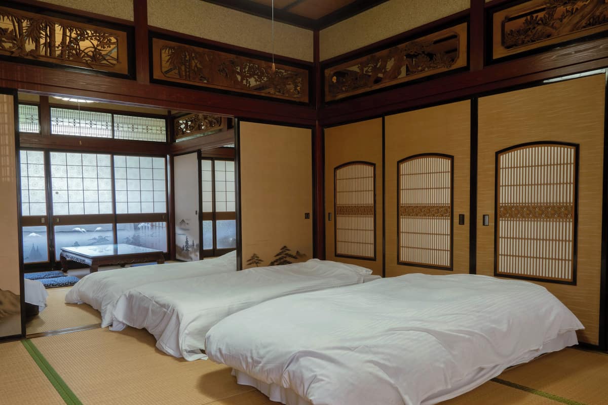 A traditional Japanese-style room with tatami flooring, two beds, sliding doors, and a view of a mountainous landscape through the windows.