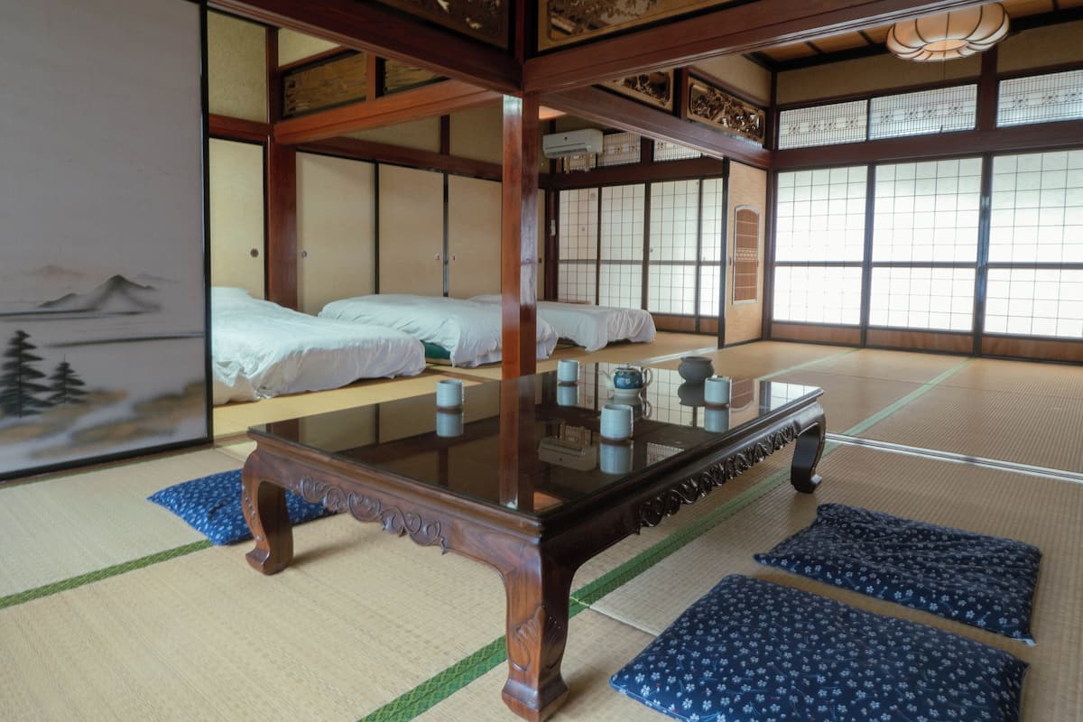 A traditional Japanese room with tatami flooring, a low wooden table, and two tatami mats with pillows.