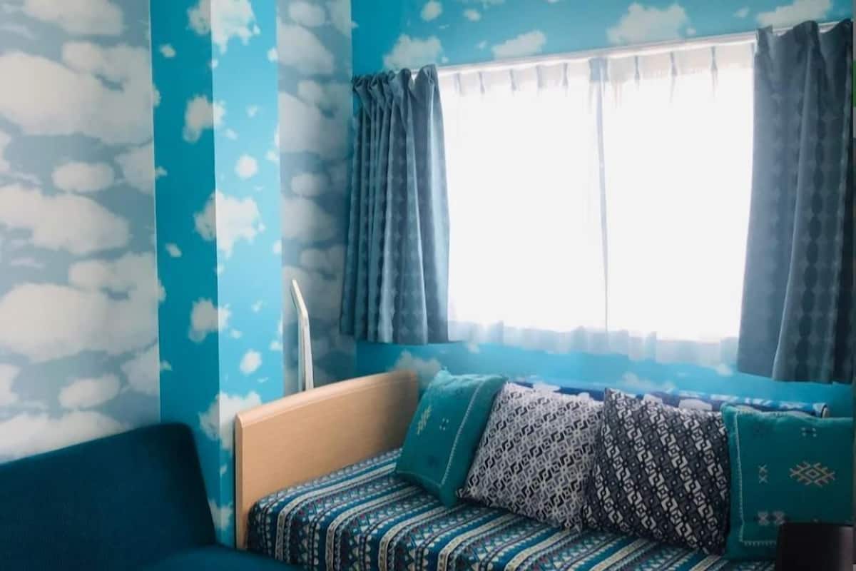 Una habitación con pared azul, una ventana con cortinas, un sofá con cojines estampados y un cabecero de madera.