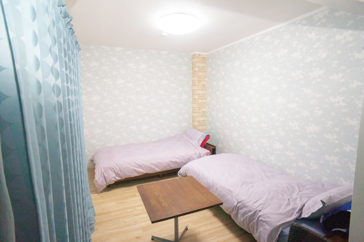 A small room with two single beds, a wooden table, and a brick accent wall.