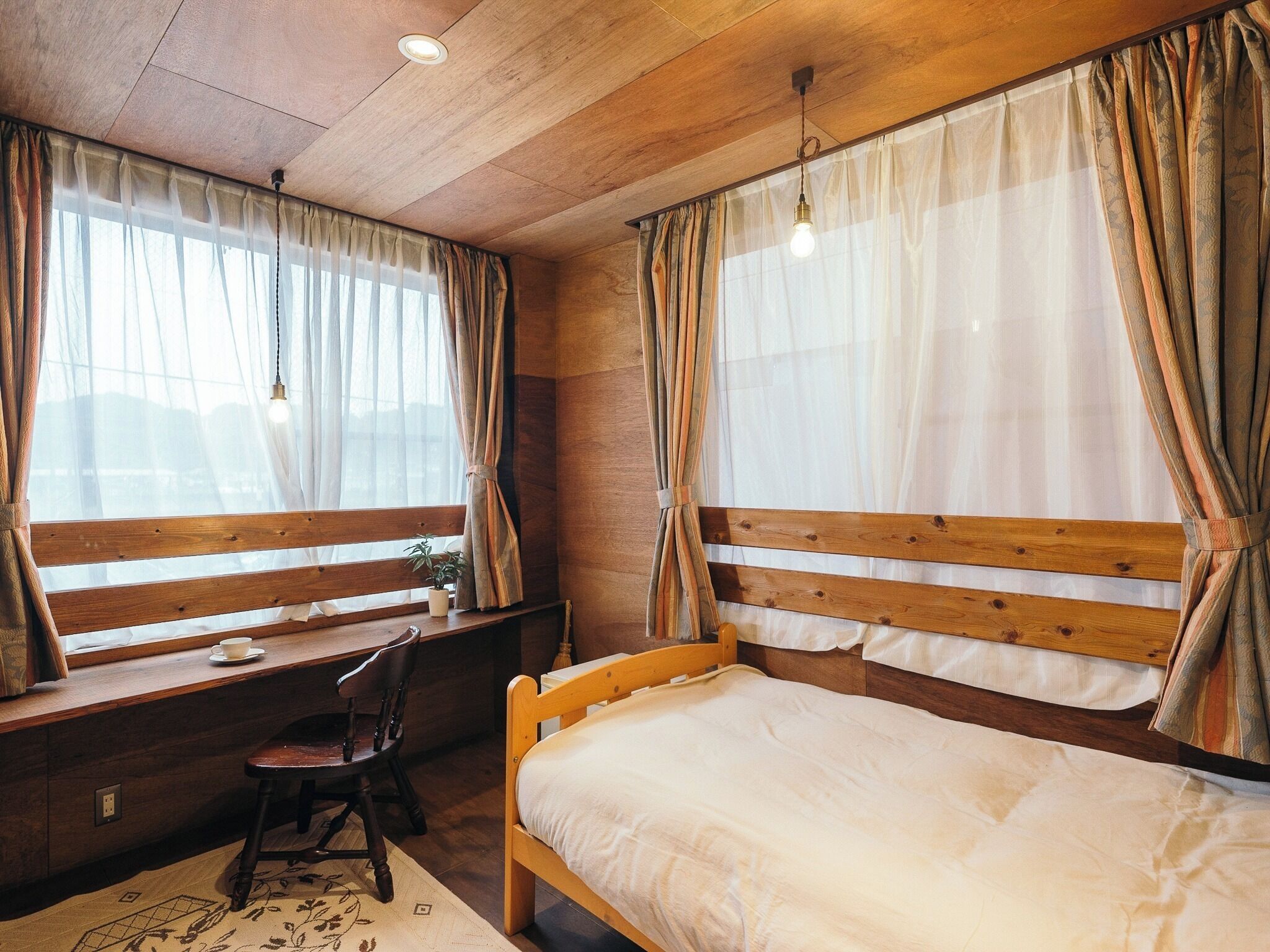 A bedroom with a wooden bed, a desk with a chair, and a window with curtains.