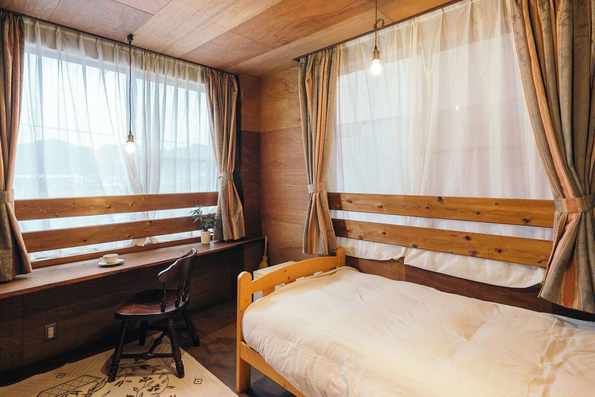 A bedroom with a wooden bed, a desk with a chair, and a window with curtains.