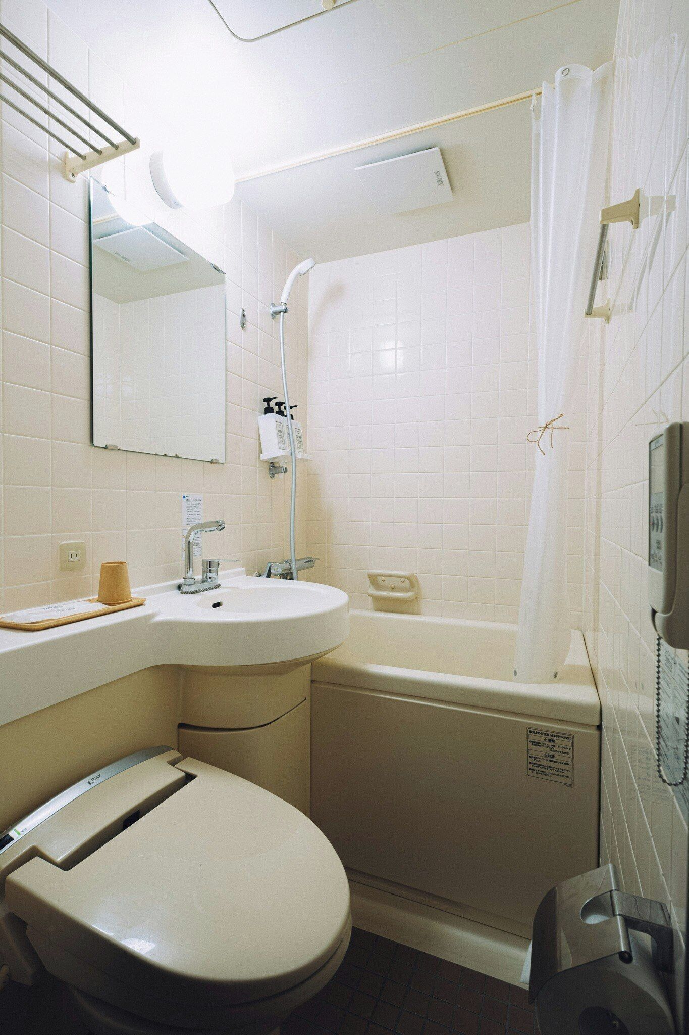 A bathroom with a toilet, sink, shower, and a telephone.