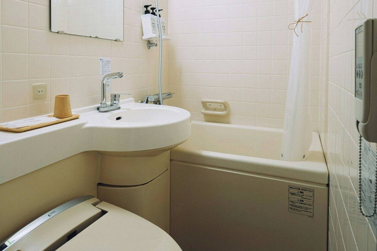 A bathroom with a toilet, sink, shower, and a telephone.