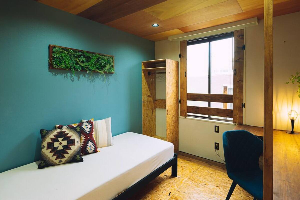 A bedroom with a bed, a window, a plant, and a wardrobe.