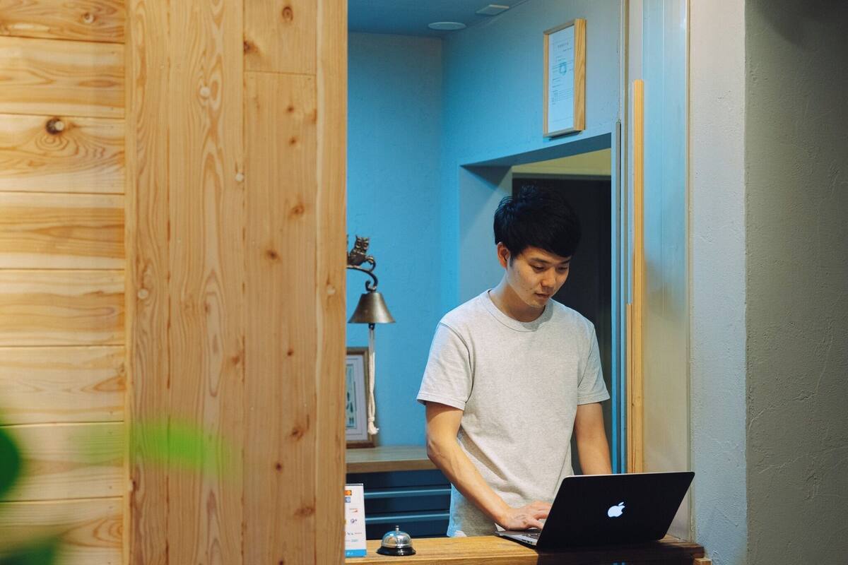 A person using a laptop in a room with wooden paneling and a blue wall.