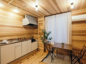 Un interior de madera con cocina, mesa de comedor, sillas, una planta en maceta y una ventana con cortinas.