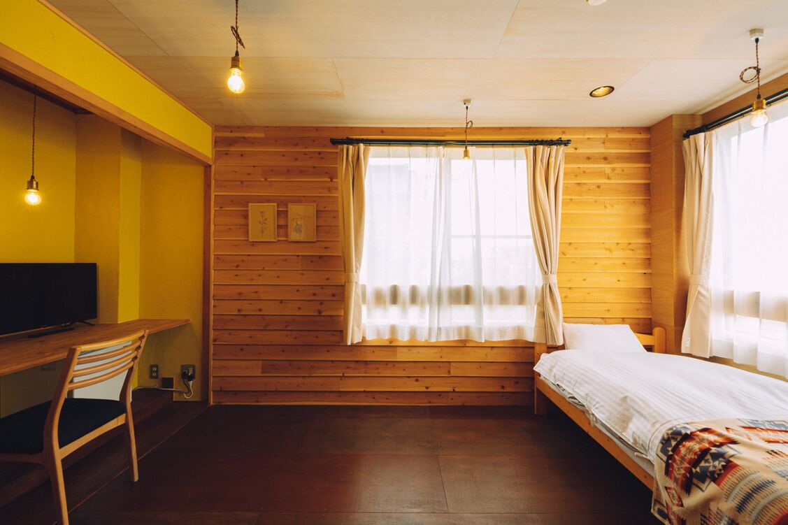 Ein Zimmer mit einer Holzwand, einem Bett, einem Schreibtisch mit Stuhl und einem Fernseher.